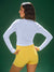 Woman wearing a white long-sleeve top and yellow shorts against a green background