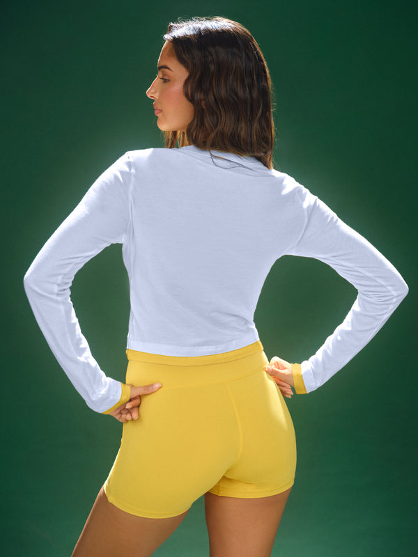 Woman wearing a white long-sleeve top and yellow shorts against a green background