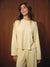 A woman modeling a pale yellow striped two-piece lounge set consisting of a long-sleeve top and matching pants, set against a dark wood-paneled background. <model-info>Kalia wears a size XS and is 5’9”, 23” waist, 32B bust.</model-info>
