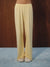 Yellow and white striped wide-leg lounge pants worn by a model, paired with beige slippers, standing on a blue carpet against a dark wood panel background.