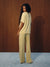 A woman stands with her back to the camera wearing a matching pale yellow short-sleeve top and wide-leg pants set with a small repeating geometric pattern, set against a dark wood-paneled wall and a light blue floor. <model-info>Gardner wears a size S and is 5’10”, 25” waist, 32½” bust.</model-info>