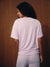 A woman shown from behind wearing a light lavender and white horizontally striped short-sleeve t-shirt and matching striped pants, standing against a dark brown wood-paneled background.