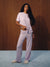 A woman modeling a light lavender ribbed lounge set consisting of a short-sleeve t-shirt and matching wide-leg pants, standing against a dark wood-paneled wall on a light blue carpet. <model-info>Gardner wears a size S and is 5’10”, 25” waist, 32½” bust.</model-info>