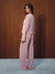 A woman wearing a light pink two-piece pajama set with a small white polka dot pattern, standing in profile against a dark wood-paneled wall.