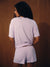 A woman shown from behind wearing a matching light lavender and white striped short-sleeve t-shirt and shorts set, standing against a dark wood-paneled background.