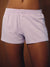 A close-up of a person wearing light lavender and white striped boxer-brief style shorts with a button placket and elastic waistband, shown against a warm brown studio background. <model-info>Gardner wears a size S and is 5’10”, 25” waist, 32½” bust.</model-info>