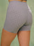 Close-up back view of a person wearing high-waisted gray athletic shorts with a small dark polka dot pattern, against a soft green background. <model-info>Raine wears a size M and is 5’8”, 29½” waist, 34” bust.</model-info>