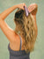 Back view of SET polka dot claw clip showcasing its dark purple design securing long hair against a muted green background