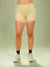 A model's lower body wearing light yellow high-waisted athletic shorts with a small black polka dot pattern, paired with black socks and white sneakers, against a light green studio backdrop.