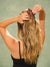 Woman securing long wavy hair with a brown polka dot SET claw clip against a green background