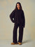 A woman modeling a dark brown lounge set consisting of a long-sleeve mock-neck sweatshirt and matching wide-leg sweatpants, paired with tan suede boots against a textured beige studio backdrop. <model-info>Kushi wears a size S and is 5'8, 24” waist, 32C bust.</model-info>