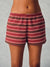 A person wearing striped lounge shorts in burgundy, olive green, and white, shown from the waist to mid-thigh against a plain light gray studio background.