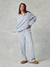 A woman modeling a light blue lounge set consisting of a long-sleeve half-zip pullover and matching wide-leg sweatpants, paired with brown slippers, against a textured gray studio background. <model-info>Kushi wears a size S and is 5'8, 24” waist, 32C bust.</model-info>