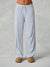 A person wearing light blue wide-leg lounge pants with a white drawstring waist, paired with tan slippers, shown from the waist down against a neutral gray studio background.