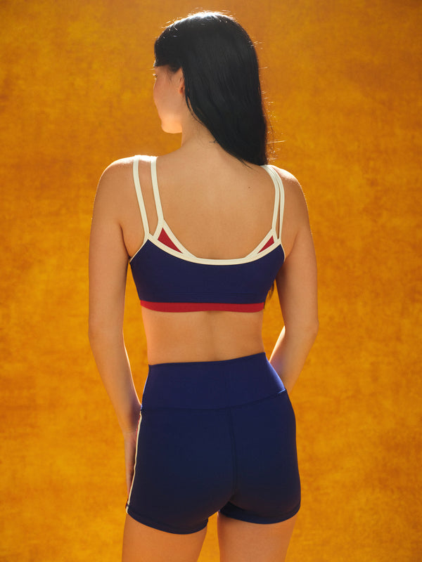 Woman wearing a blue sports bra and shorts set against an orange background