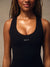 A close-up of a woman wearing a black athletic tank top with the word 'SET' printed in white on the chest, against a neutral beige background.