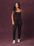 A woman modeling a black activewear set consisting of a tank top and matching leggings with side chain detailing, paired with white sneakers, standing against a textured dark purple studio backdrop. <model-info> Christina wears a size L and is 5’9, 29½” waist, 36" bust.</model-info> 