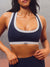 A close-up of a woman wearing a navy blue sports bra with white trim and a white underband featuring the brand  <model-info>Alana wears a size M and is 5’8”, 28” waist, 35" bust.</model-info>name 'SET'.