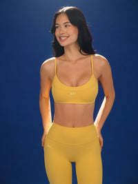 Woman wearing a yellow sports bra and leggings against a blue background 