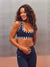 A woman modeling a navy blue activewear set featuring a sports bra with white striped trim and matching high-waisted leggings with a white side stripe. The brand name 'SET' is visible on the  <model-info>Scha'leigh wears a size XS and is 5’8”, 24” waist, 32B bust.</model-info>thigh.
