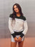 A woman modeling a color-blocked long-sleeve athletic sweatshirt with white, dark green, and light blue stripes, paired with a matching white athletic skirt, set against a textured gray studio background. <model-info>Jelene wears a size XS and is 5’7”, 23” waist, 32AB bust.</model-info>