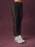 Black high-waisted leggings with a vertical gold chain-link pattern down the side, modeled with white socks and white sneakers against a textured dark purple studio backdrop.