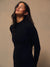 A woman wearing a black long-sleeve athletic zip-up jacket, shown in a side profile against a warm beige studio background. <model-info>Jelene wears a size XS and is 5’7”, 23” waist, 32AB bust.</model-info>