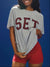Person wearing a gray t-shirt with 'SET' printed on it against a blue background <model-info>Umi wears a size S and is 5’8½”, 23½” waist, 32B bust.</model-info>