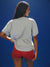 Person wearing a gray t-shirt and red shorts against a blue background