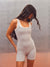 A woman modeling a light gray ribbed tank top and matching shorts set against a textured gray wall with a warm brown floor. <model-info>Jelene wears a size XS and is 5’7”, 23” waist, 32AB bust.</model-info>