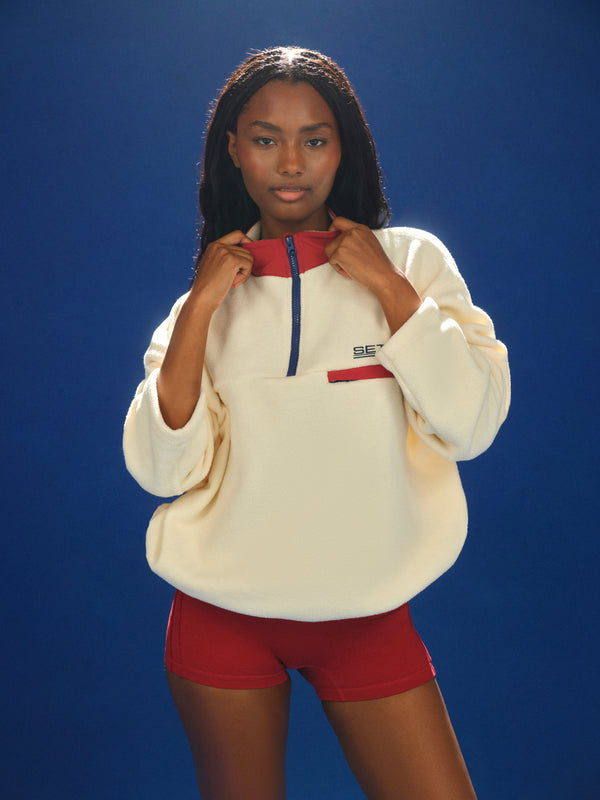 Person wearing a large beige sweatshirt with a red interior against a blue background 