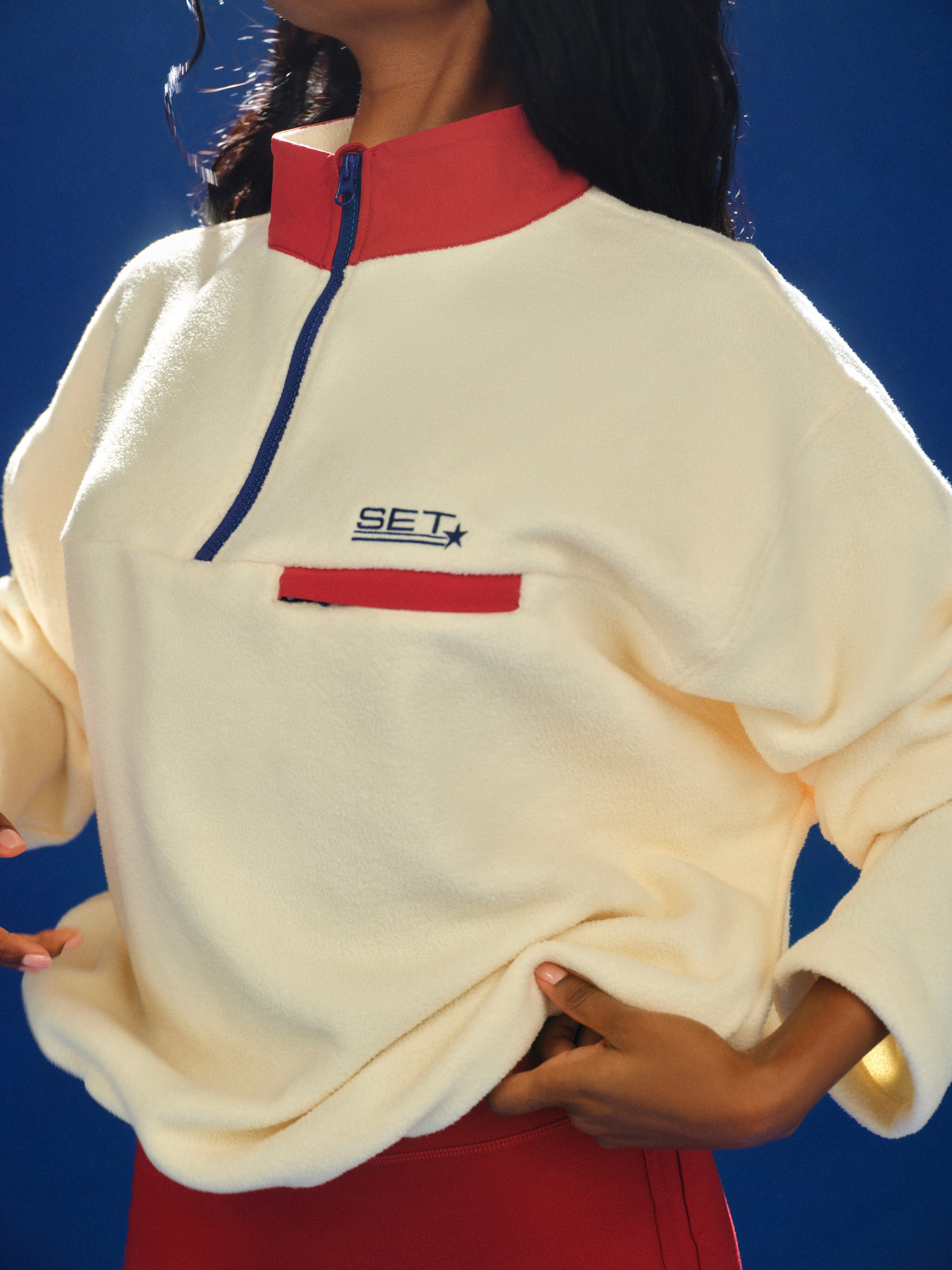 Person wearing a white fleece pullover with red and blue accents against a blue background