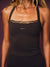 A close-up of a woman wearing a black athletic tank top with a small white 'SET' logo on the chest, posed against a dark purple studio background. <model-info> Andrea wears a size S and is 5’9”, 25½” waist, 32” bust.</model-info>