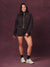 A woman modeling a dark brown zip-up hoodie and matching shorts set standing against a textured dark purple studio backdrop.