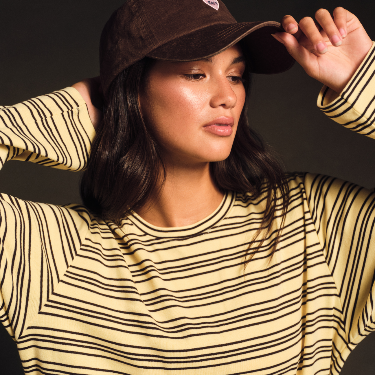 Woman wearing a yellow and black striped shirt with a brown cap on a dark background