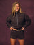 A woman modeling a dark brown zip-up sweatshirt and matching shorts set with lettering on a textured dark purple studio background. <model-info> Andrea wears a size XS and is 5’9”, 25½” waist, 32” bust.</model-info>