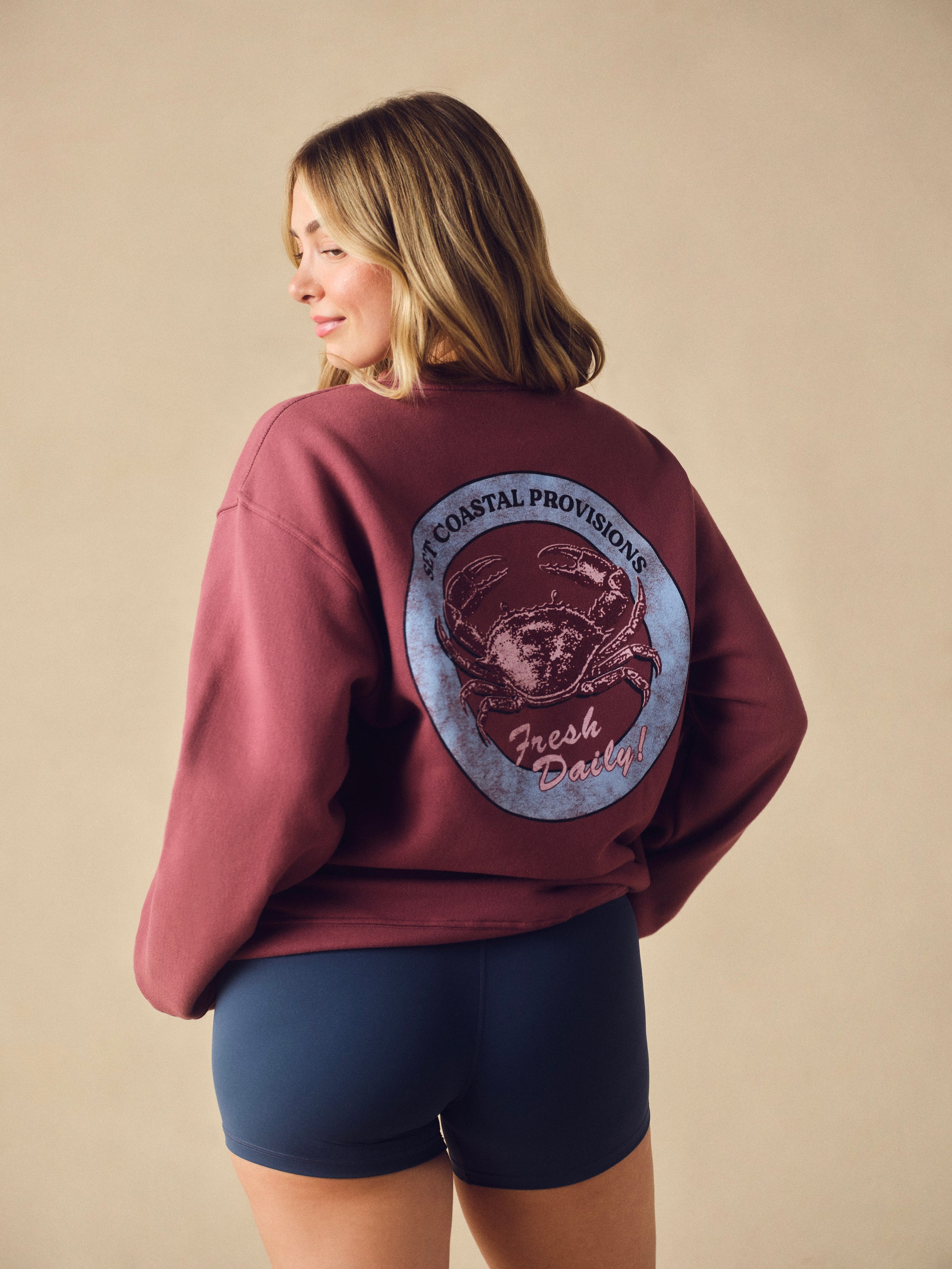 A woman wearing a oversized dusty rose crewneck sweatshirt with a 'SET' graphic on the back. <model-info>Raine wears a size M/L and is 5’8”, 29½” waist, 34” bust.</model-info>