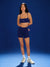 Woman wearing a navy blue sports bra and shorts set on a blue background