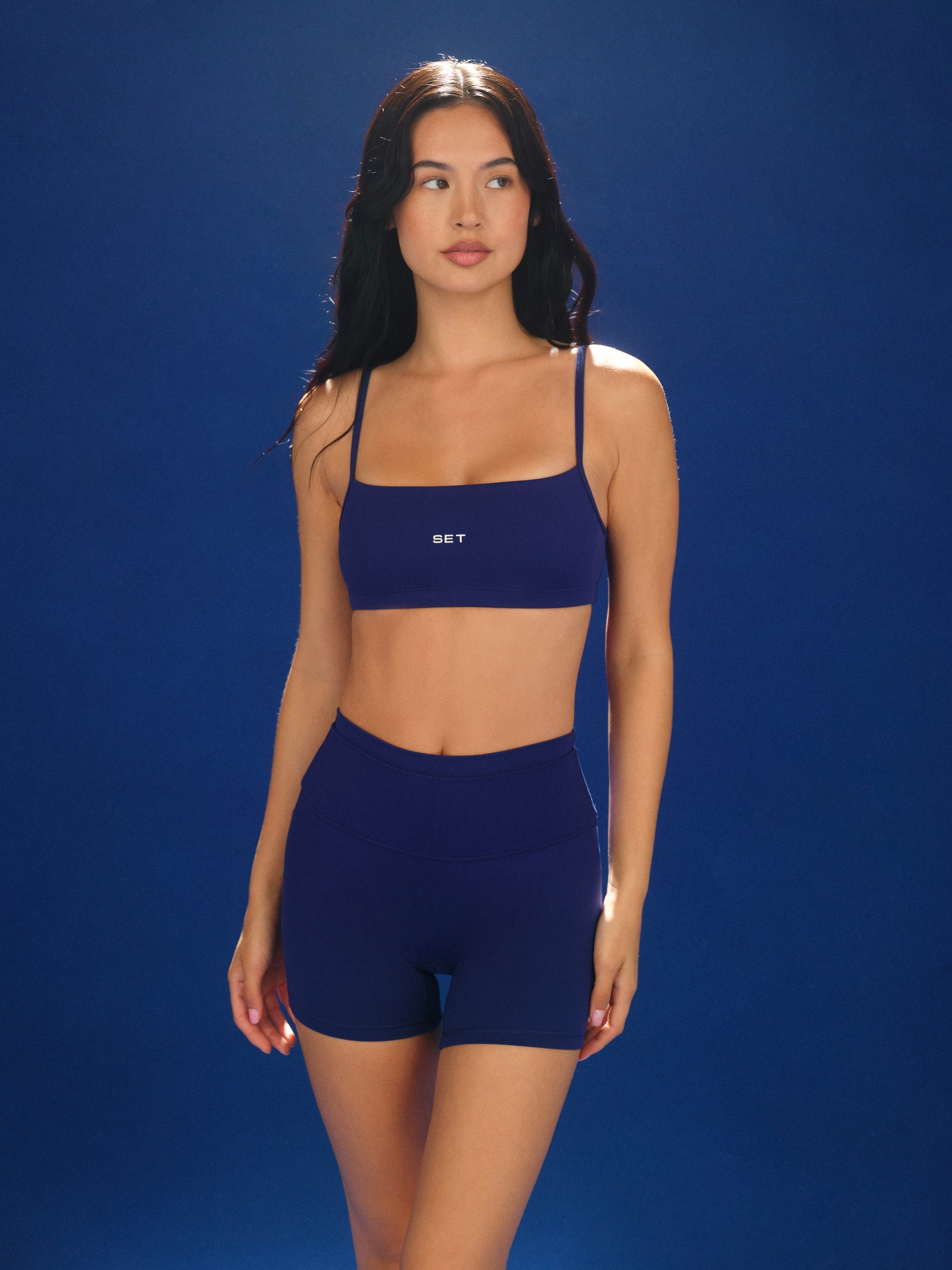 Woman wearing a navy blue sports bra and shorts set against a blue background