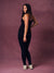 A woman modeling a black sleeveless jumpsuit with zebra detailing, standing against a textured mauve studio backdrop.