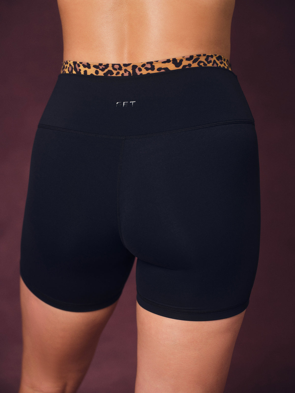Rear view of a model wearing black high-waisted athletic biker shorts with a leopard print waistband and a small silver logo on the center back.