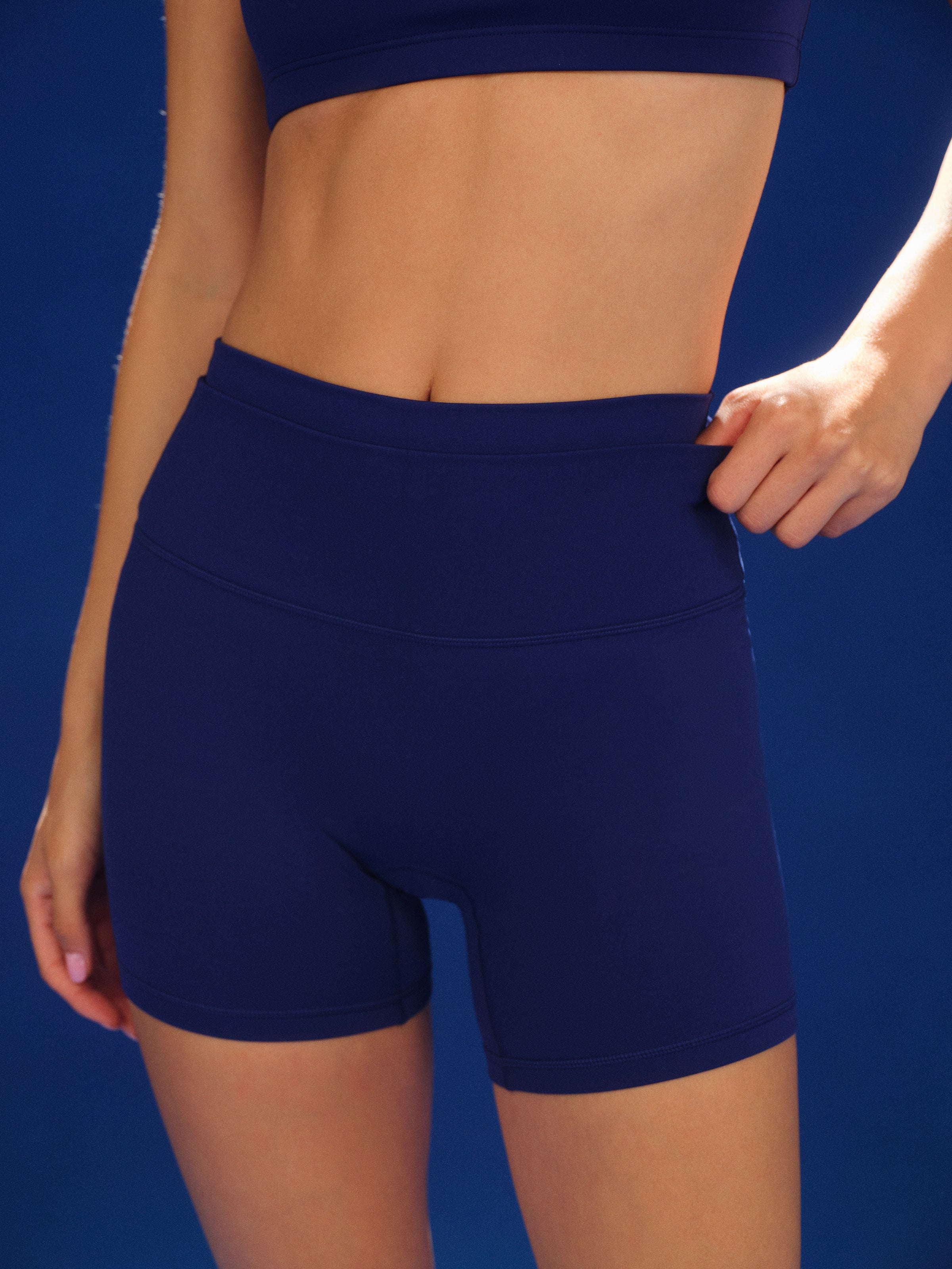 Person wearing navy blue athletic shorts against a blue background