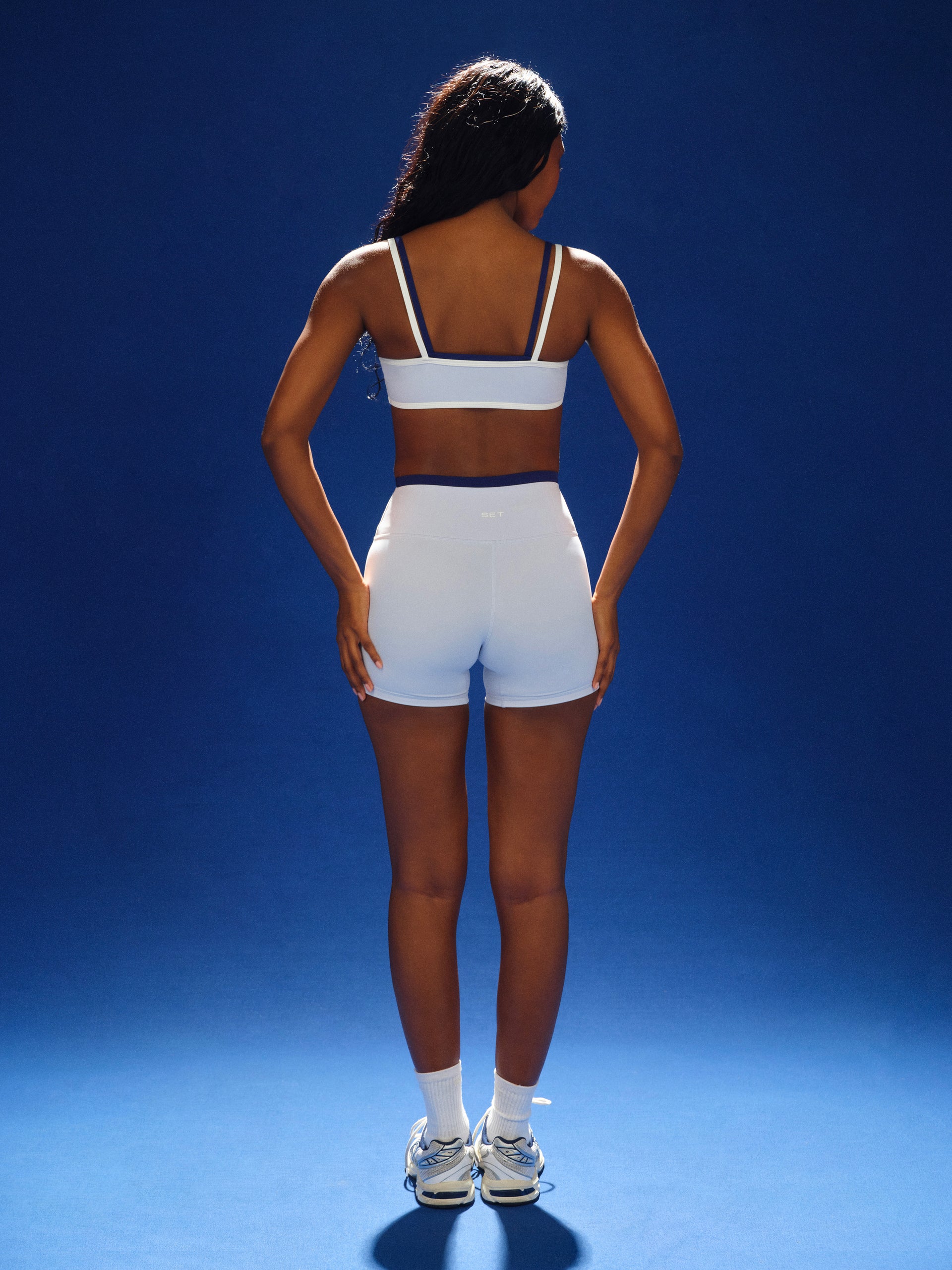 Person wearing a white sports bra and shorts on a blue background