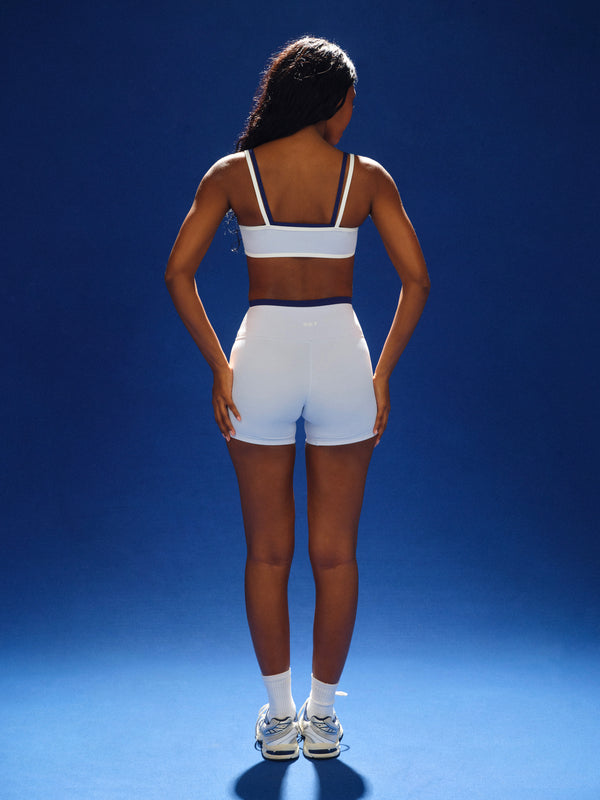 Person wearing a white sports bra and shorts on a blue background