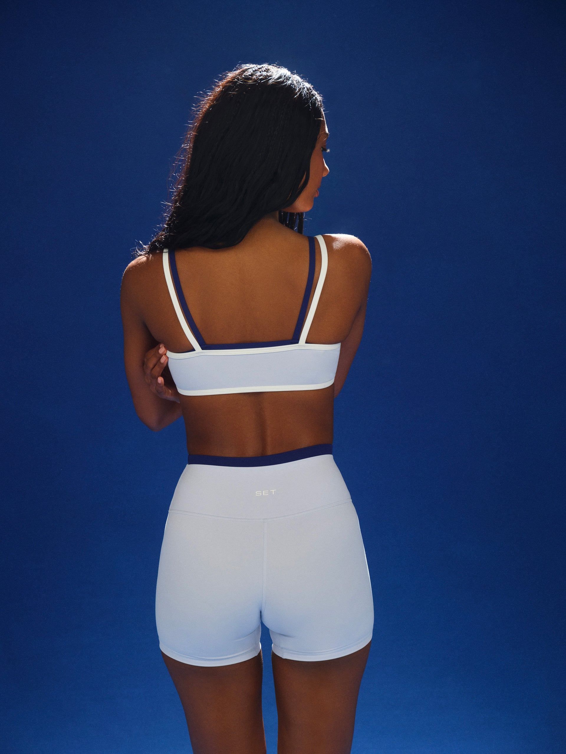 Woman wearing a white sports bra and shorts against a blue background