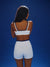 Woman wearing a white sports bra and shorts against a blue background