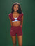 Woman wearing a maroon sports bra and shorts set on a green background <model-info>Umi wears a size XS and is 5’8½”, 23½” waist, 32B bust.</model-info>