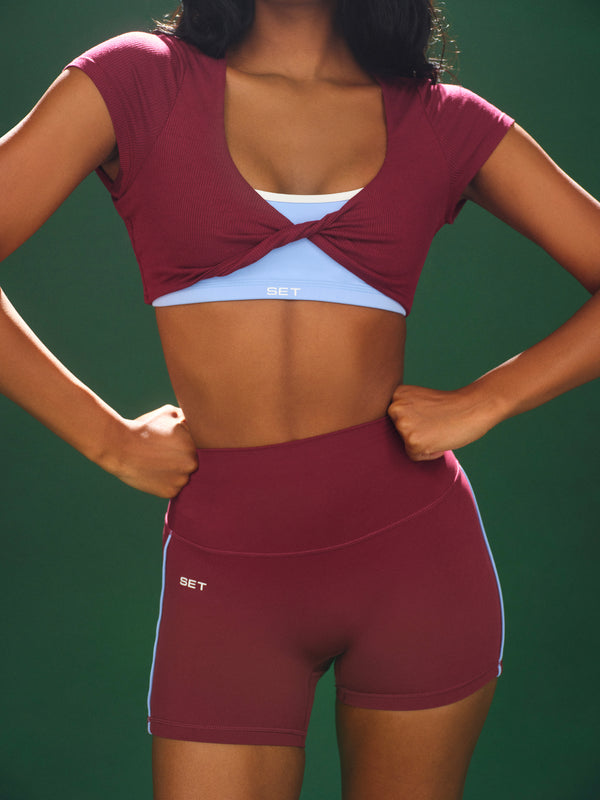 Person wearing a maroon sports bra and shorts set with a green background