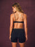 A woman shown from the back wearing a black leopard-print sports bra and matching black athletic shorts against a textured dark purple studio background.