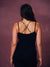 A woman viewed from behind wearing a black camisole with a black and white patterned crisscross strap design on the back, set against a textured mauve background.